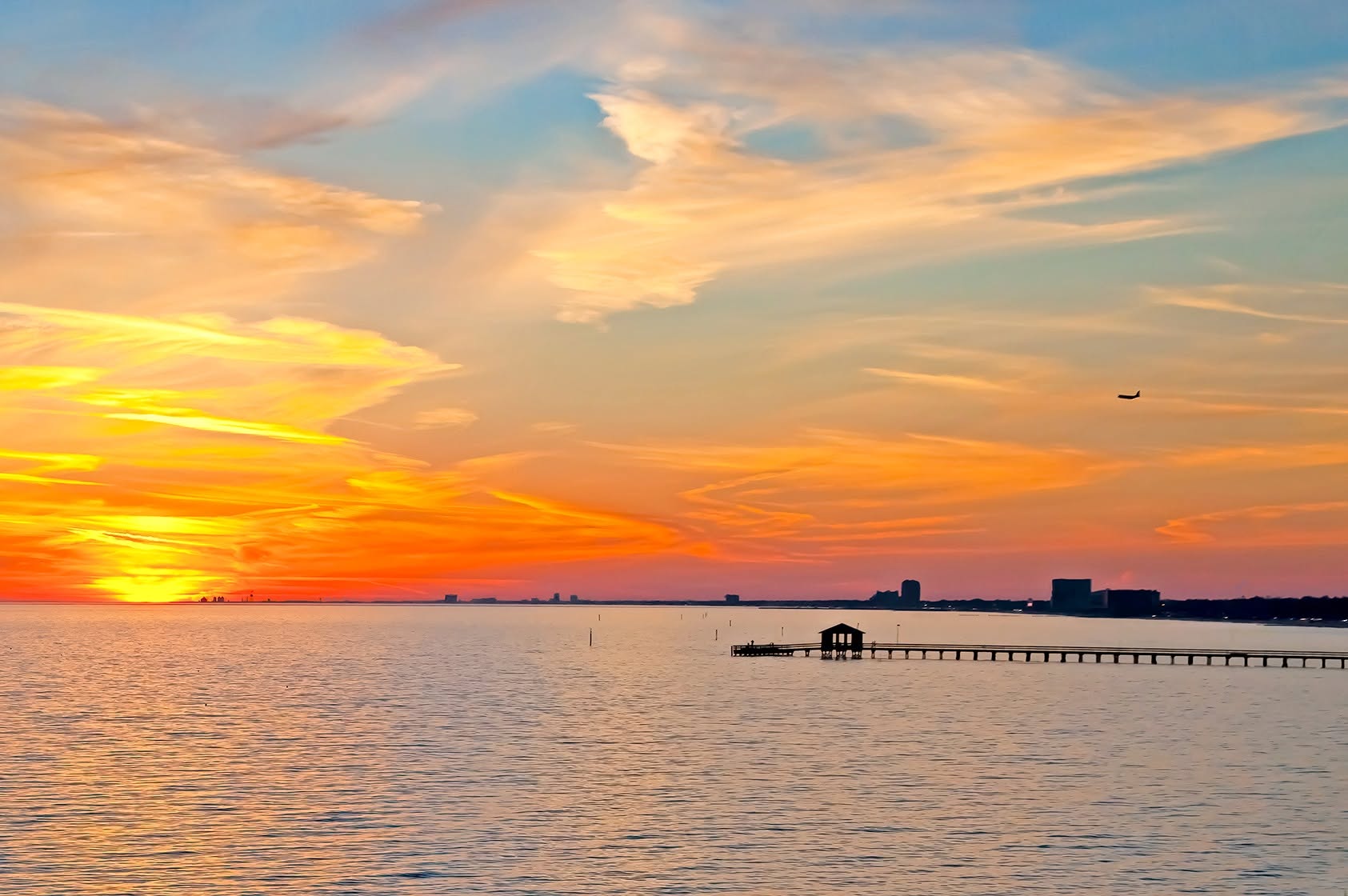 Sunset over coastal water with a pier and distant shoreline